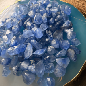 A collection of raw, unpolished blue sapphire gemstones displayed on a decorative blue and gold plate.